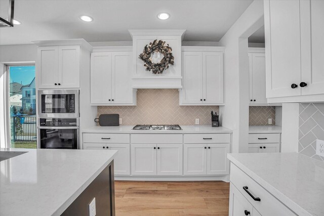 kitchen featuring white cabinetry, light stone counters, light hardwood / wood-style flooring, stainless steel gas stovetop, and backsplash