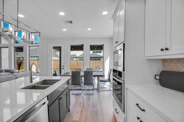 kitchen featuring sink, white cabinetry, light wood-type flooring, hanging light fixtures, and appliances with stainless steel finishes