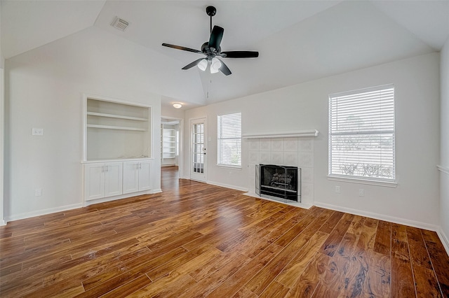 unfurnished living room featuring built in shelves, visible vents, vaulted ceiling, wood finished floors, and a tile fireplace