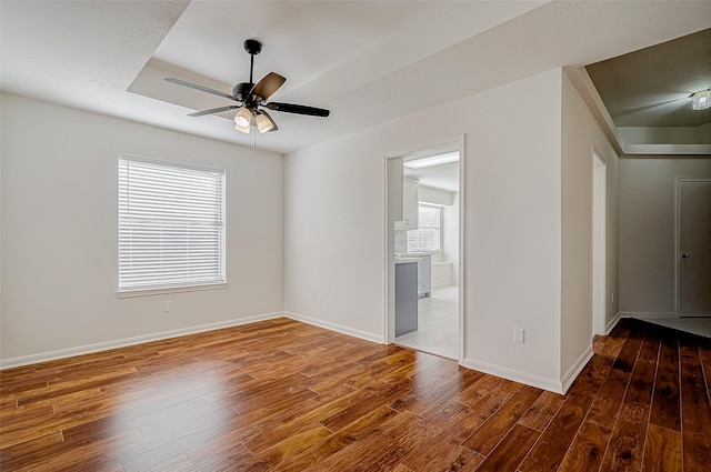 spare room with hardwood / wood-style flooring, baseboards, a raised ceiling, and a ceiling fan