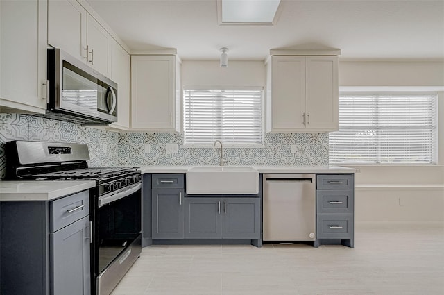 kitchen with gray cabinets, light countertops, backsplash, appliances with stainless steel finishes, and a sink