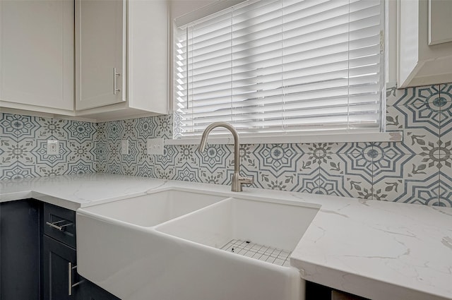 kitchen featuring light stone counters, a sink, white cabinets, and decorative backsplash