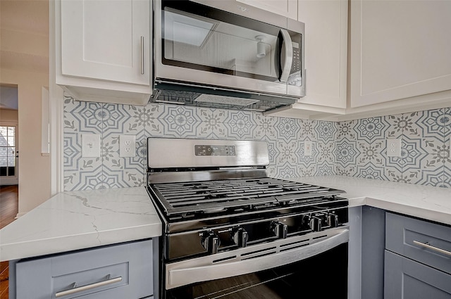 kitchen with appliances with stainless steel finishes, gray cabinetry, decorative backsplash, and light stone counters