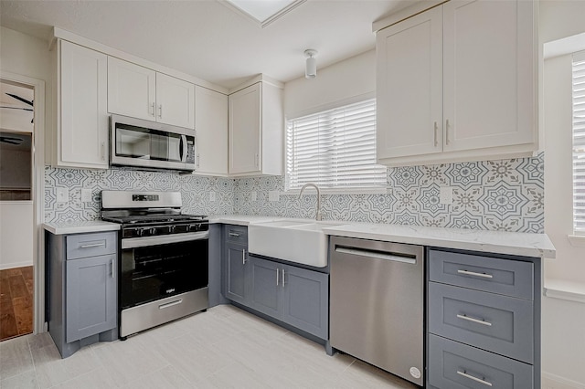 kitchen with backsplash, appliances with stainless steel finishes, gray cabinets, and a sink