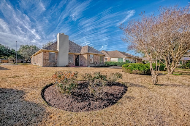 exterior space with a chimney, a lawn, and brick siding