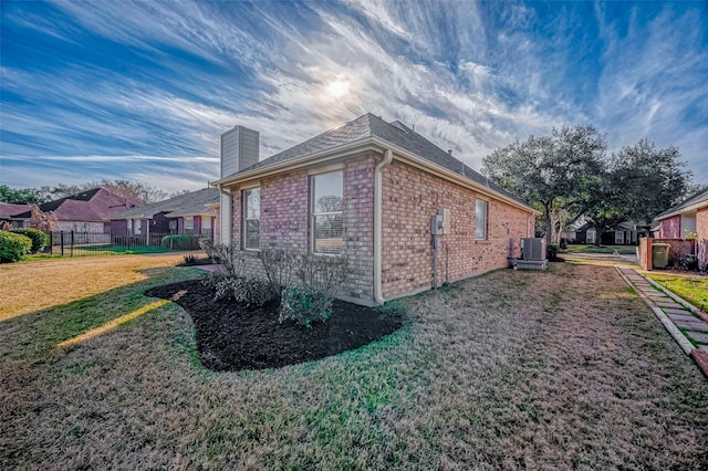 view of side of property featuring central AC unit, a chimney, fence, a yard, and brick siding