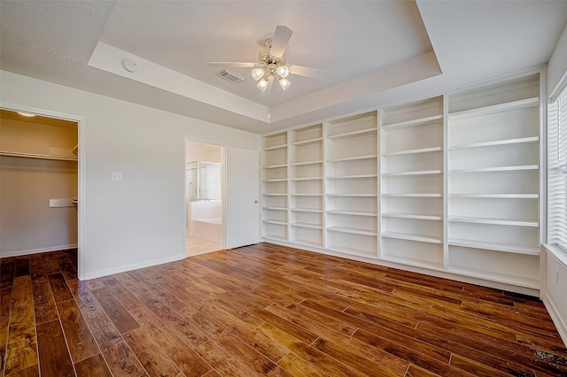 unfurnished bedroom featuring a tray ceiling, a walk in closet, visible vents, hardwood / wood-style floors, and baseboards