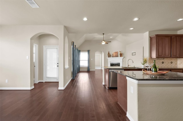 kitchen featuring sink, dark stone countertops, stainless steel dishwasher, dark hardwood / wood-style floors, and decorative backsplash