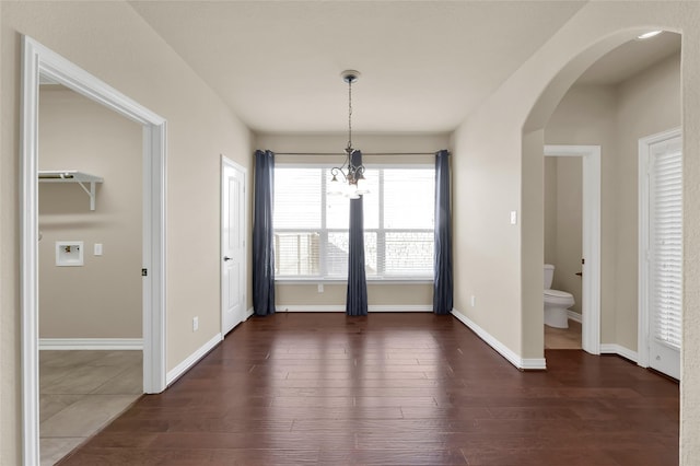 unfurnished dining area with arched walkways, dark wood finished floors, and baseboards