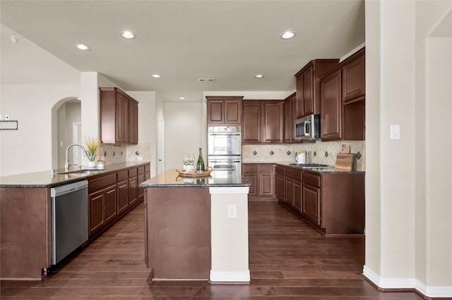 kitchen with a peninsula, appliances with stainless steel finishes, dark wood-type flooring, and a sink