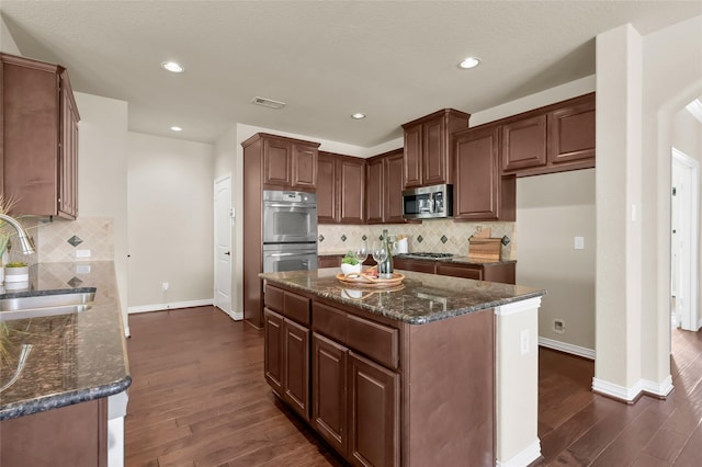 kitchen with visible vents, a kitchen island, appliances with stainless steel finishes, dark wood-style flooring, and a sink