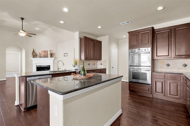 kitchen with arched walkways, a fireplace, appliances with stainless steel finishes, open floor plan, and a kitchen island