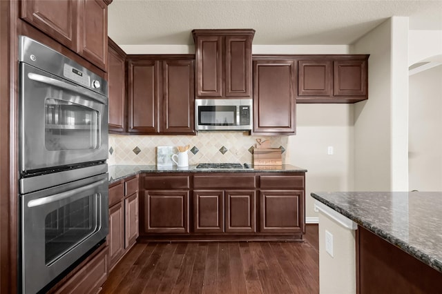 kitchen with a textured ceiling, stainless steel appliances, dark wood-style flooring, backsplash, and dark stone counters