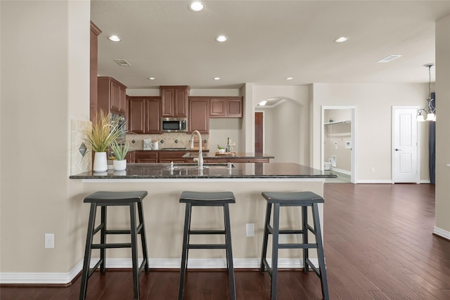 kitchen with a peninsula, a sink, brown cabinets, dark stone counters, and stainless steel microwave