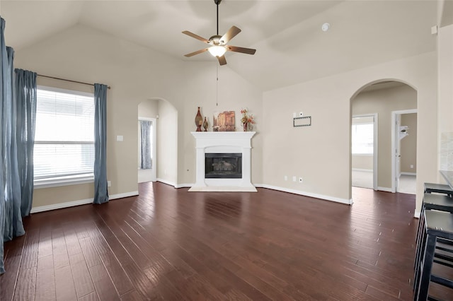 unfurnished living room featuring dark wood-type flooring, arched walkways, a glass covered fireplace, and vaulted ceiling