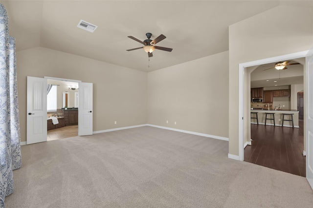 interior space with ceiling fan, ensuite bathroom, vaulted ceiling, and light carpet