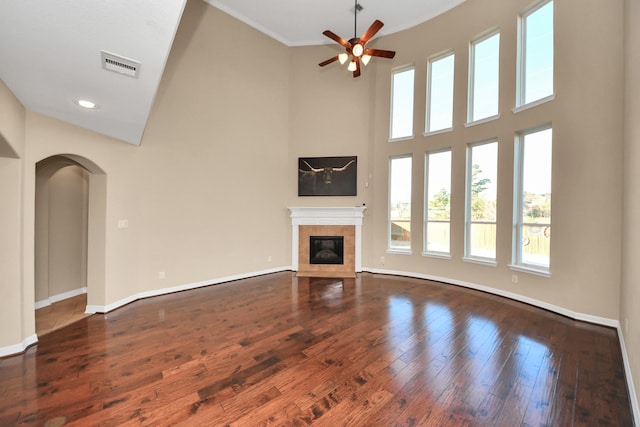 unfurnished living room with ceiling fan, wood-type flooring, a high ceiling, and a tile fireplace