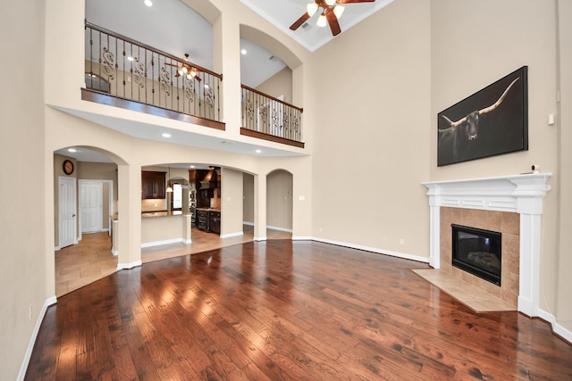 unfurnished living room featuring hardwood / wood-style floors, a towering ceiling, ceiling fan, and a tiled fireplace