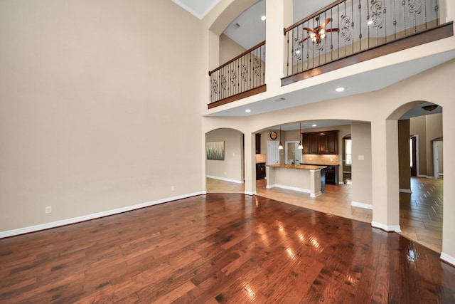 unfurnished living room with hardwood / wood-style flooring, ceiling fan, crown molding, and a high ceiling