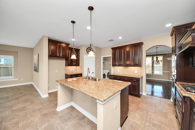 kitchen with backsplash, sink, decorative light fixtures, independent washer and dryer, and an island with sink