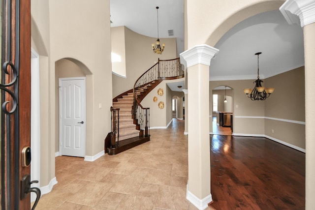 entryway with a notable chandelier, ornamental molding, a high ceiling, and ornate columns