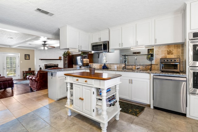 kitchen with a textured ceiling, stainless steel appliances, ceiling fan, white cabinetry, and a kitchen island