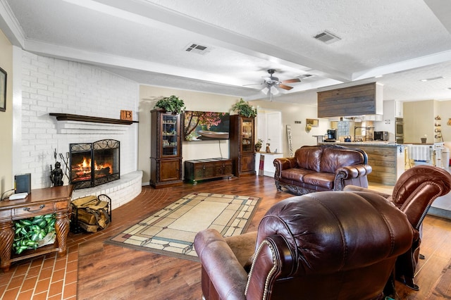 living room featuring hardwood / wood-style floors, ceiling fan, a fireplace, a textured ceiling, and beamed ceiling