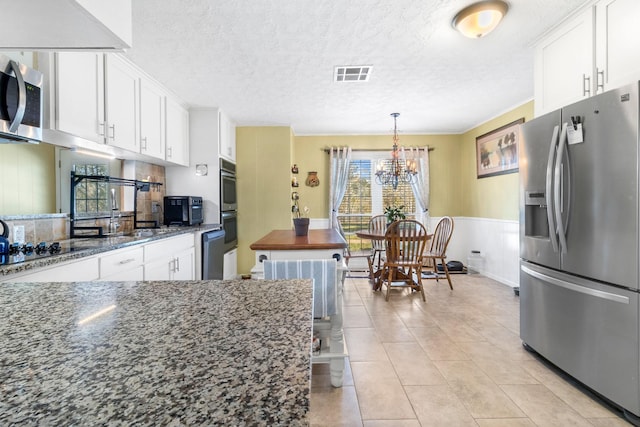 kitchen featuring white cabinets, appliances with stainless steel finishes, dark stone counters, and a notable chandelier