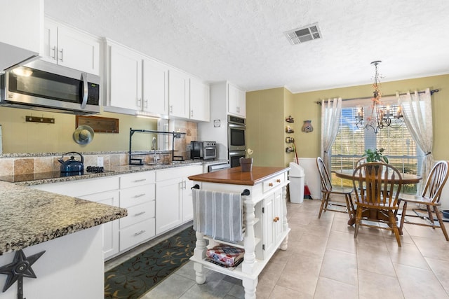 kitchen with pendant lighting, dark stone counters, white cabinets, a notable chandelier, and stainless steel appliances