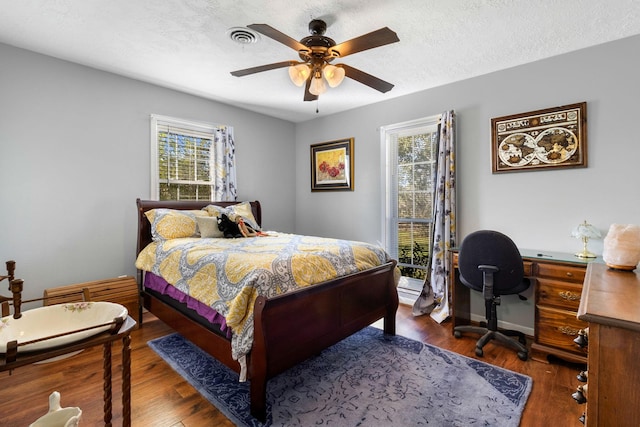 bedroom with a textured ceiling, ceiling fan, and dark wood-type flooring