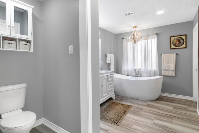 bathroom featuring an inviting chandelier, a tub to relax in, a textured ceiling, toilet, and vanity