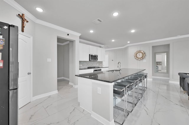 kitchen with white cabinetry, a kitchen breakfast bar, an island with sink, dark stone counters, and appliances with stainless steel finishes