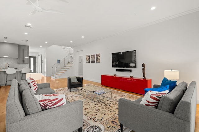 living room with ceiling fan, light wood-type flooring, ornamental molding, and sink