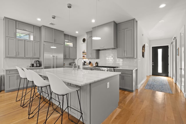 kitchen with light wood-type flooring, a kitchen island with sink, gray cabinetry, and pendant lighting