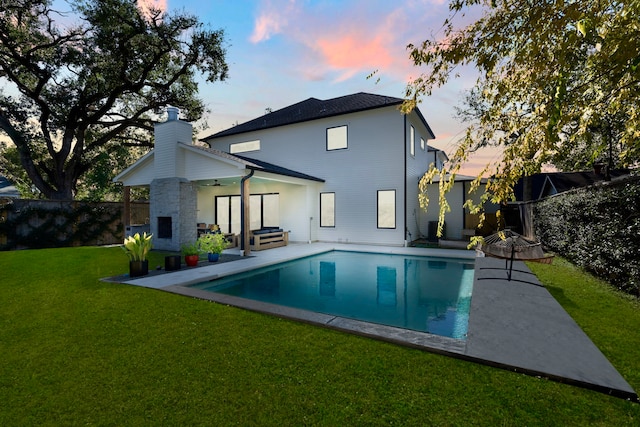 back house at dusk featuring ceiling fan, a yard, a fenced in pool, and a patio