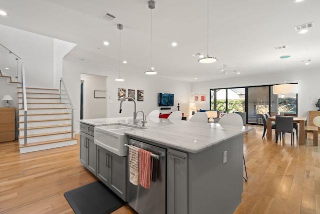 kitchen with stainless steel dishwasher, pendant lighting, gray cabinetry, and an island with sink