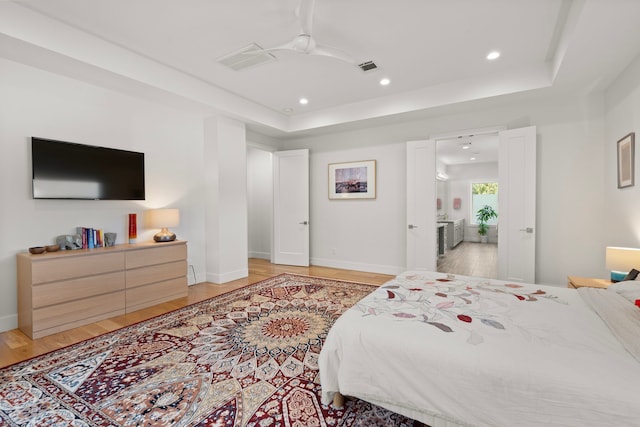 bedroom featuring ceiling fan, a tray ceiling, and light hardwood / wood-style floors