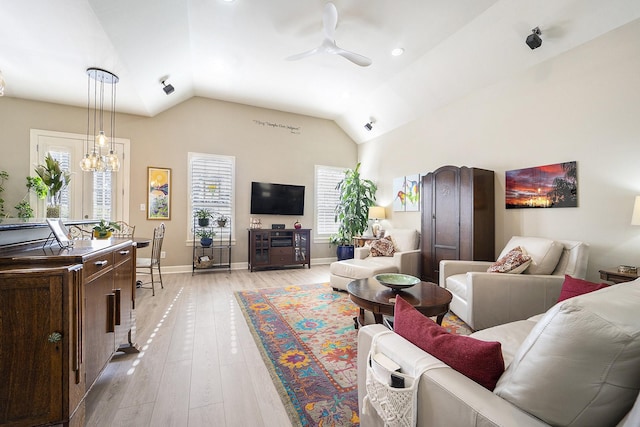 living room with ceiling fan with notable chandelier, lofted ceiling, and light hardwood / wood-style flooring