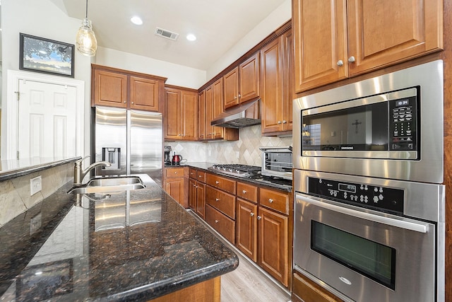 kitchen with stainless steel appliances, sink, light hardwood / wood-style flooring, decorative backsplash, and dark stone counters