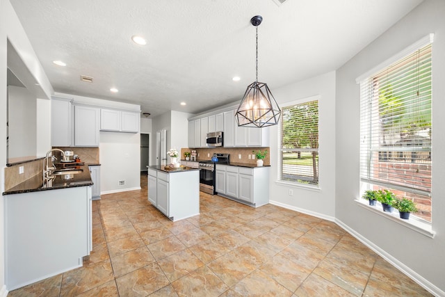 kitchen featuring white cabinetry, sink, hanging light fixtures, a kitchen island, and appliances with stainless steel finishes