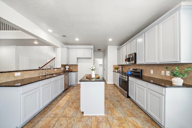 kitchen with white cabinetry, kitchen peninsula, dark stone counters, a textured ceiling, and appliances with stainless steel finishes