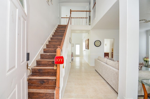 stairs with tile patterned floors, crown molding, and a high ceiling