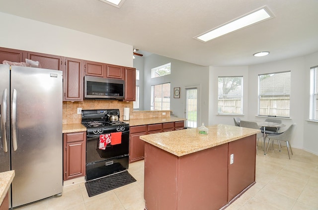 kitchen with decorative backsplash, appliances with stainless steel finishes, a kitchen island, and light tile patterned flooring