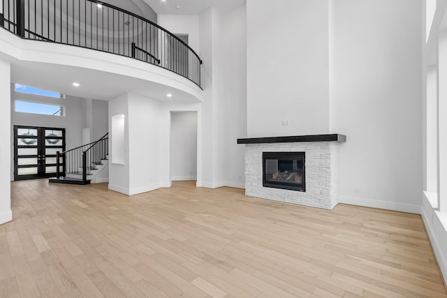 unfurnished living room featuring a towering ceiling, a fireplace, and light hardwood / wood-style flooring