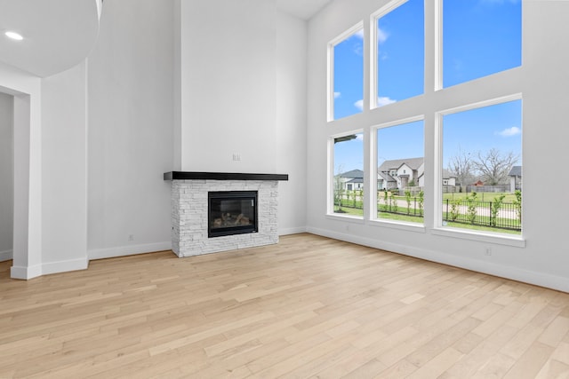 unfurnished living room featuring light hardwood / wood-style floors, a stone fireplace, and a towering ceiling