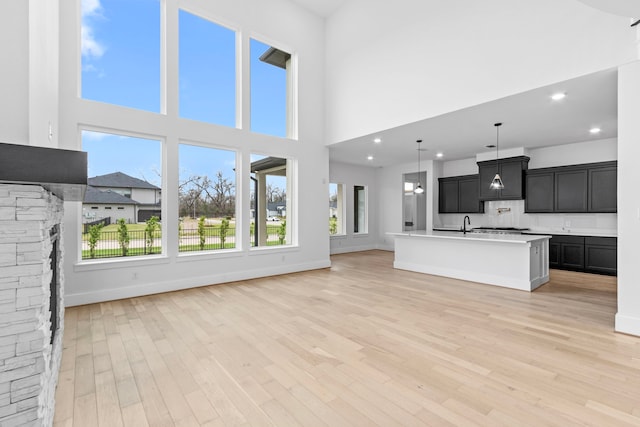 unfurnished living room featuring a stone fireplace, a towering ceiling, and light wood-type flooring