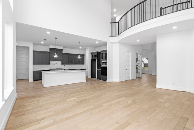 kitchen featuring sink, stainless steel oven, light hardwood / wood-style flooring, a towering ceiling, and an island with sink