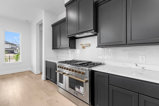 kitchen with light stone countertops, wall chimney range hood, tasteful backsplash, light hardwood / wood-style flooring, and double oven range