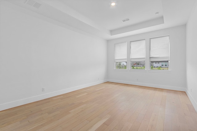 empty room featuring light hardwood / wood-style floors and a tray ceiling