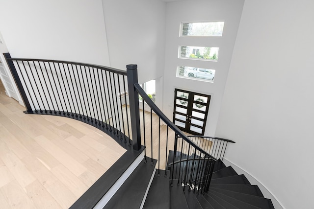 stairs with wood-type flooring, a towering ceiling, and french doors